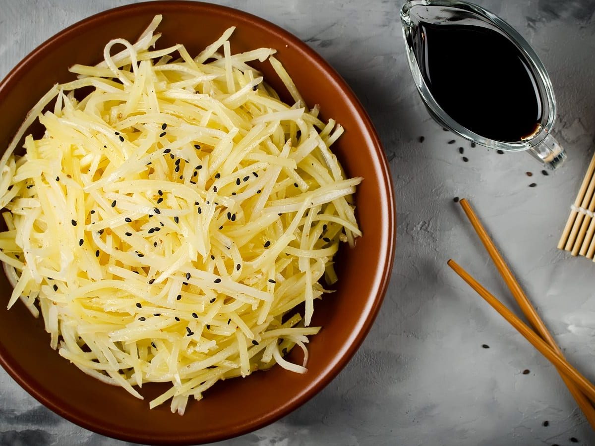 Ein brauner Teller mit chinesischem Kartoffelsalat auf einem grauen Untergrund.