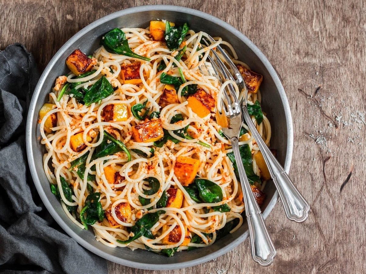 Ein Teller mit Kürbis-Pasta mit Spinat auf einem braunen Tisch.