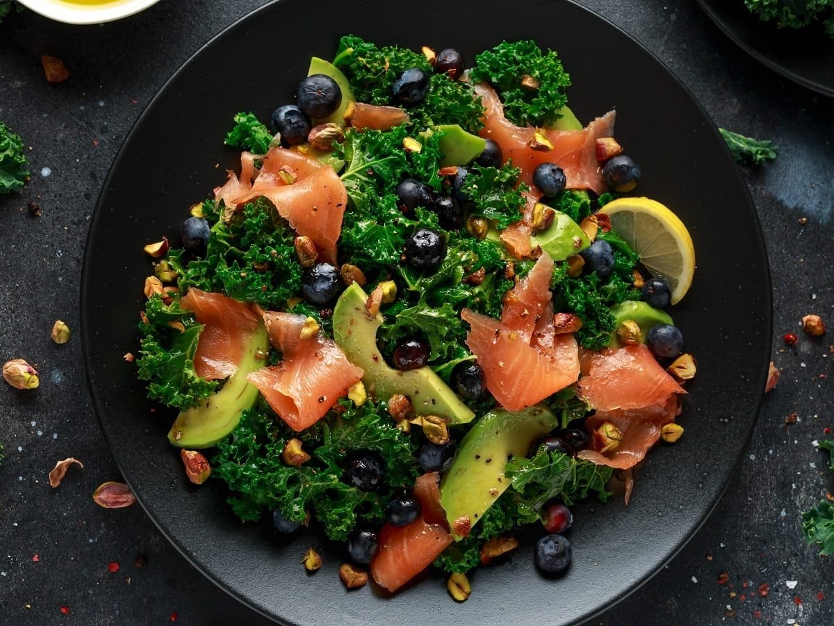 Ein schwarzer Teller mit Grünkohlsalat mit Lachs und Avocado.