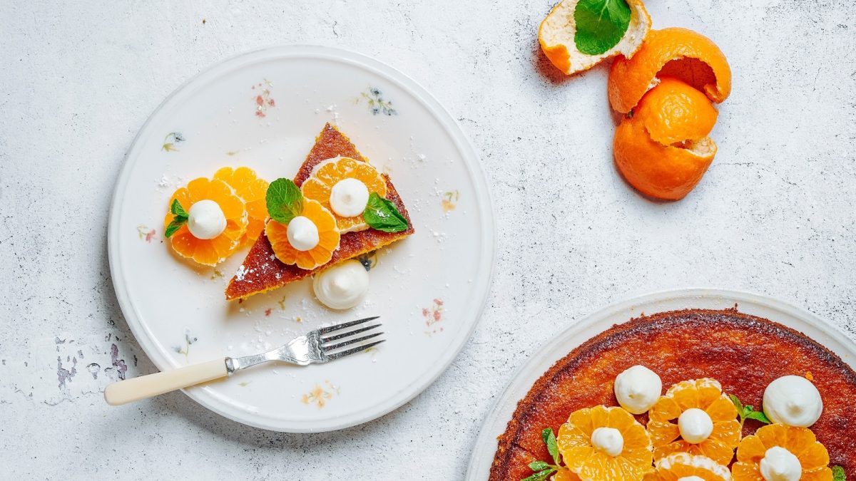 Ein weißer Teller mit Mandarinen-Mandelkuchen auf einem weißen Tisch.