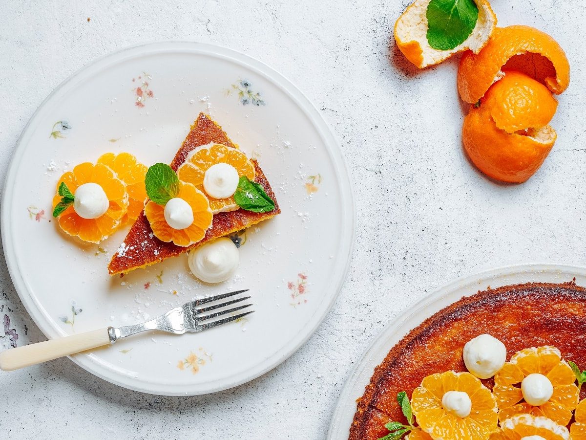 Ein weißer Teller mit Mandarinen-Mandelkuchen auf einem weißen Tisch.