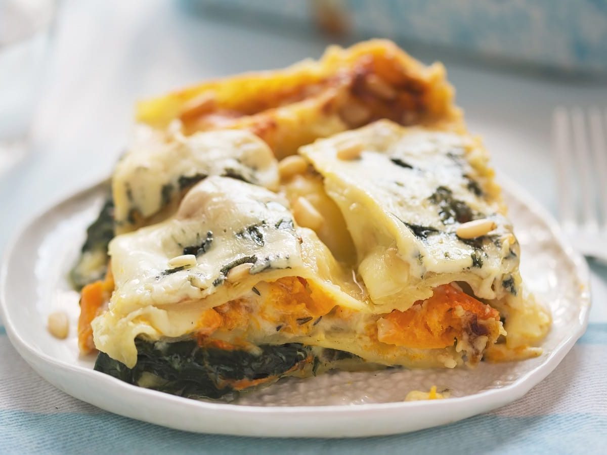 Ein Teller mit einer Portion Kürbis-Lasagne mit Spinat auf einem hellen Tisch.