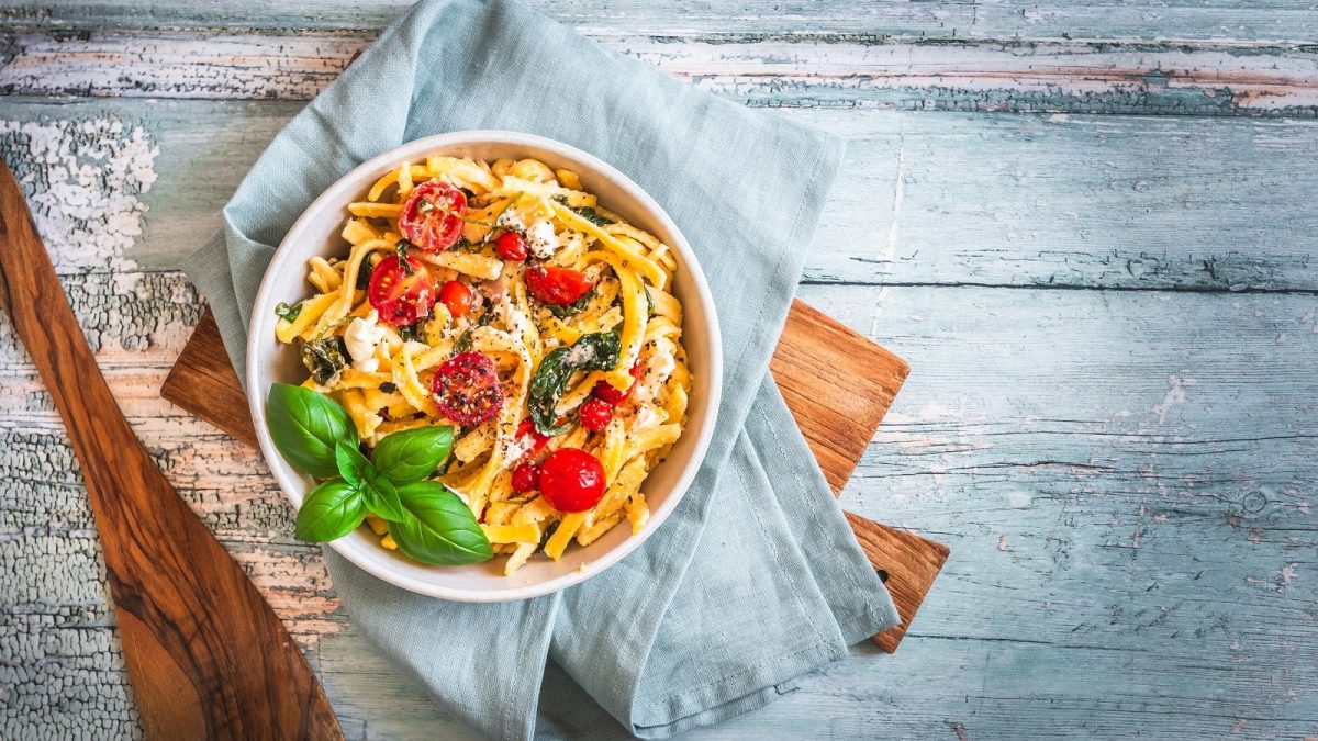 Ein Teller mit einer Portion Spätzlepfanne mit Spinat und Tomaten.