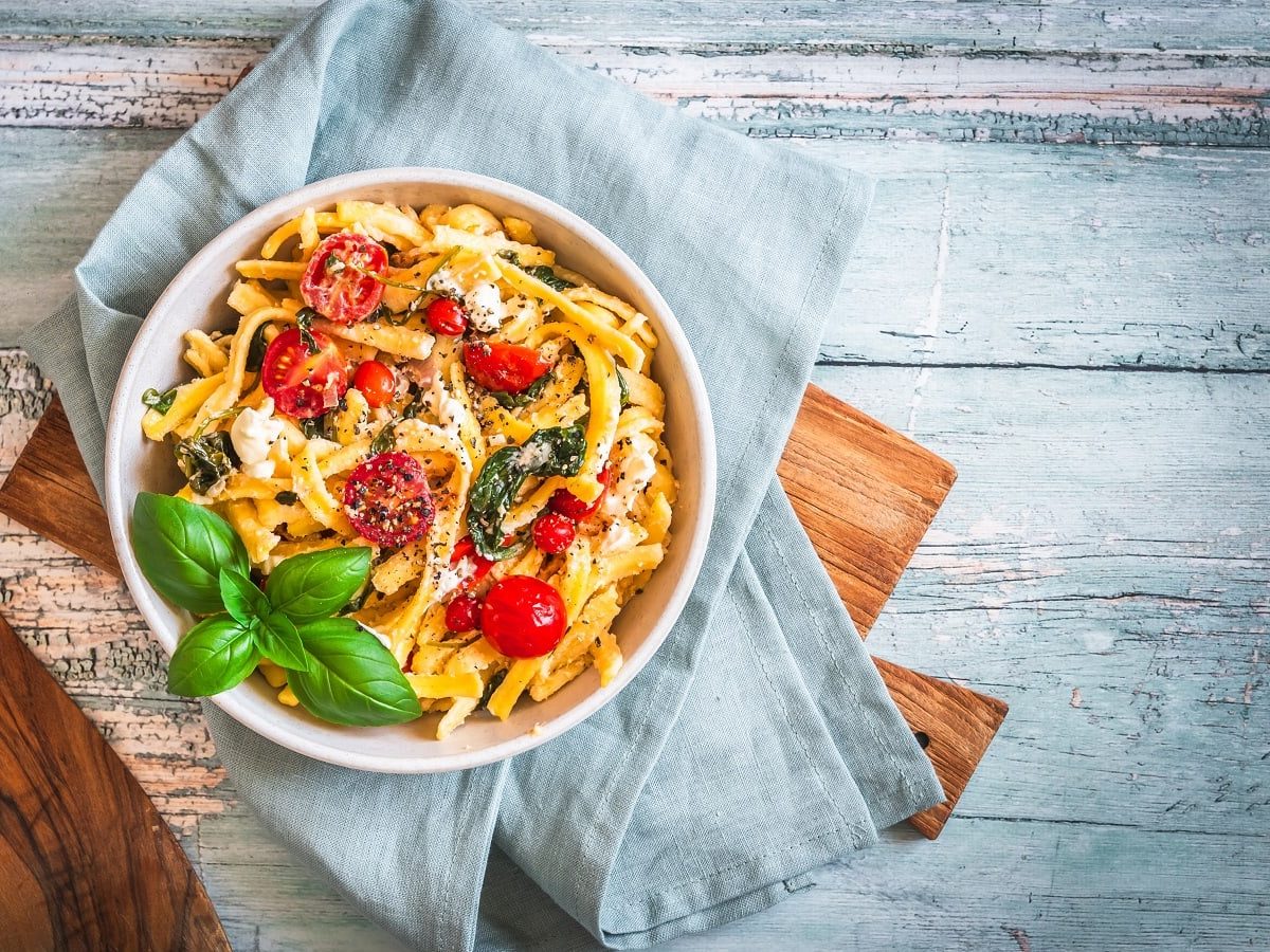 Ein Teller mit einer Portion Spätzlepfanne mit Spinat und Tomaten.