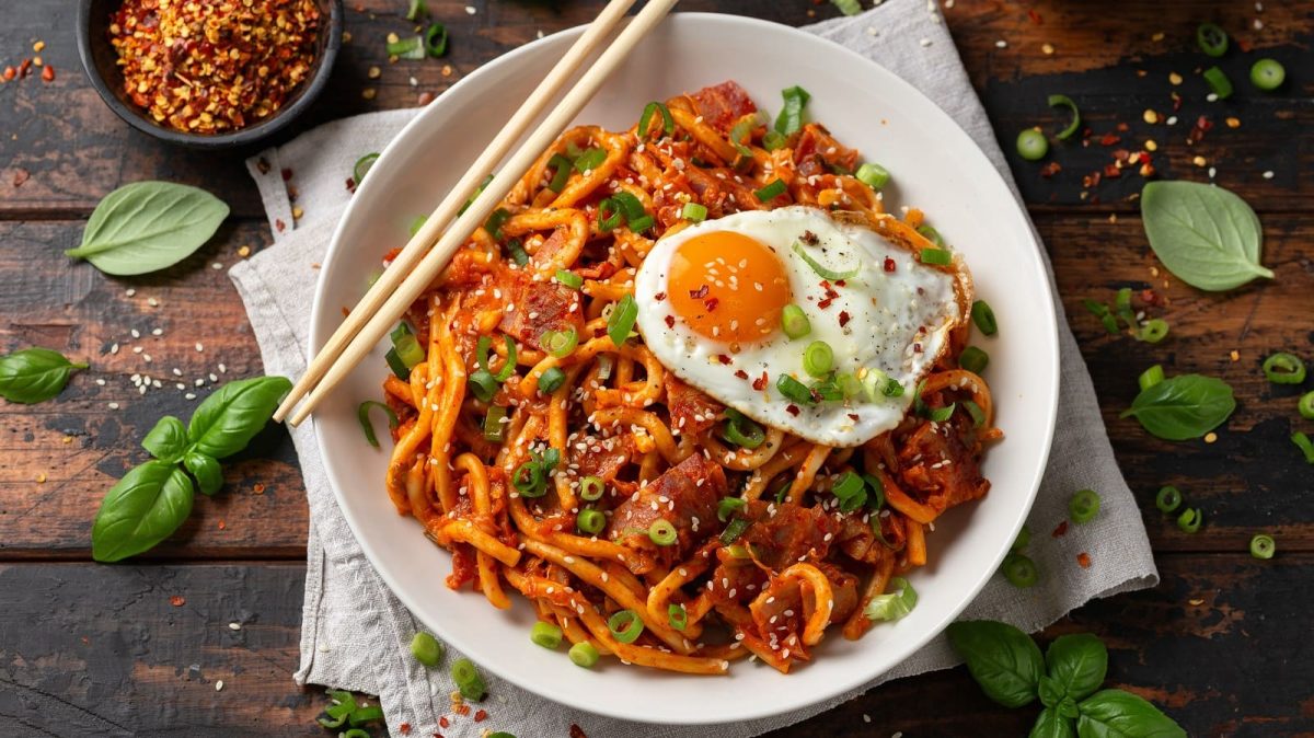 Ein weißer Teller mit gebratenen Udon-Nudeln mit Tomaten.