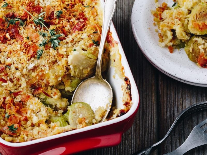 Draufsicht: Eine teilweise Ansicht eines Brüsseler Gratins mit Rosenkohl. Daneben ist ein Teller mit Brüsseler Gratin mit Rosenkohl.