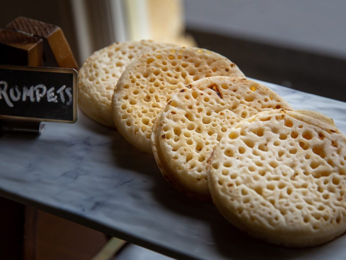 Draufsicht, schräg: 4 ofenfrische Crumpets auf einen dunklen Platte.