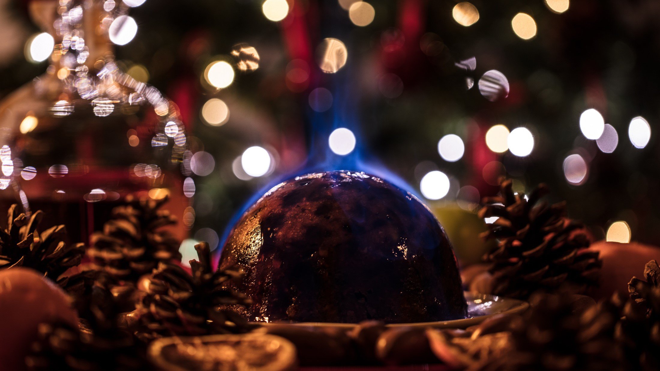 Frontal: Ein britischer Christmas Pudding der flambiert wird. Drum herum ist es weihnachtlich geschmückt.