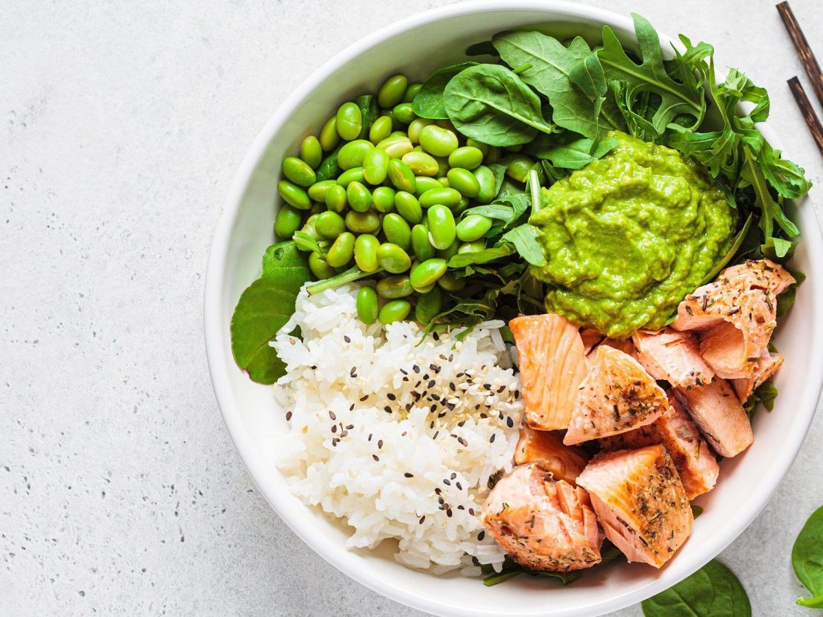 Draufsicht: Heller Untergrund, einen Edamame-Bowl mit Lachs und Esstäbchen.