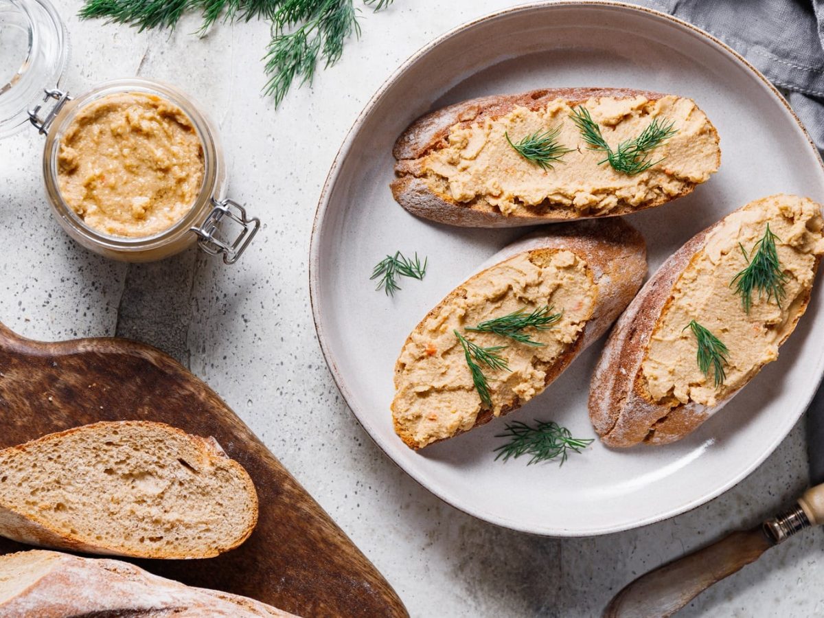 Drei Baguettescheiben mit der Feta-Walnusscreme auf einem weißen Teller und hellem Tisch direkt von oben fotografiert.