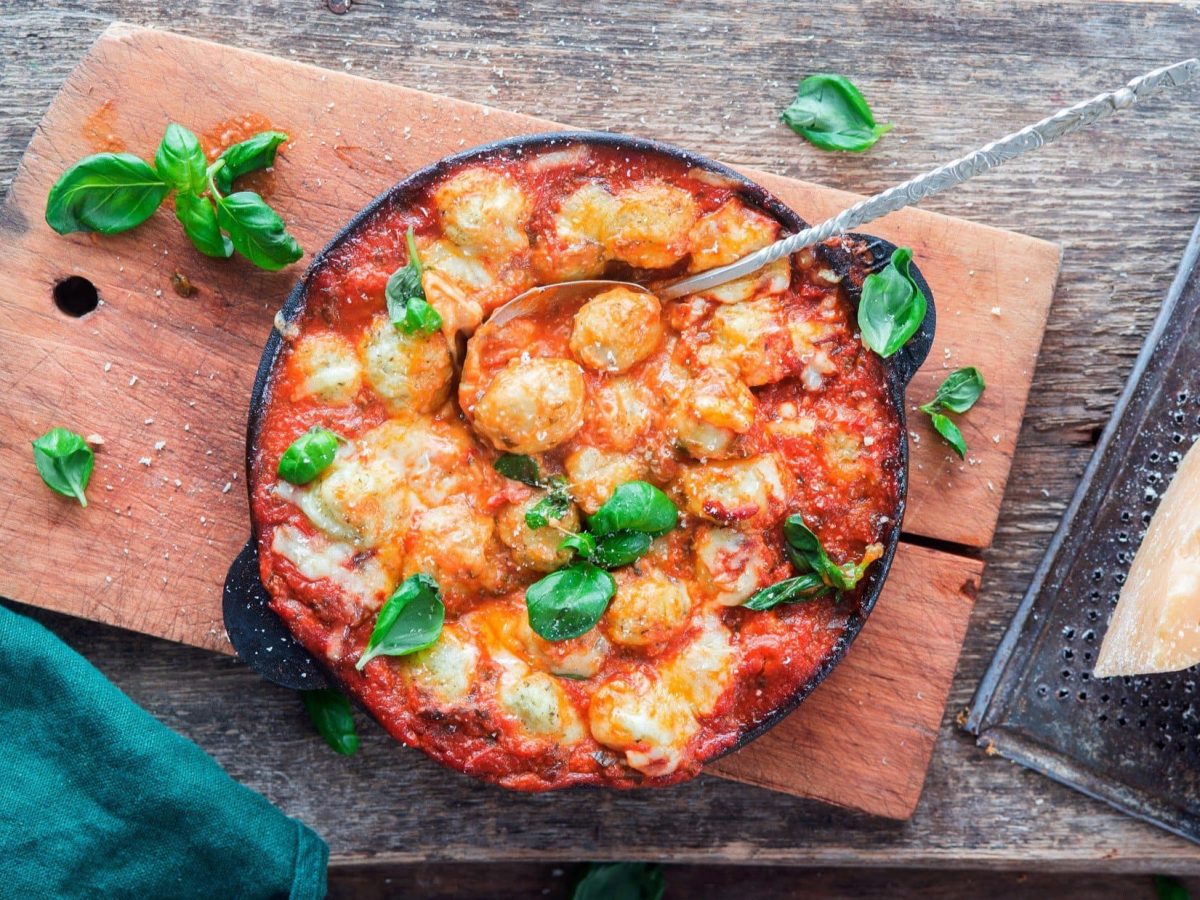 Draufsicht: ein Gnocchi-Auflauf Caprese auf einem Holzbrett.