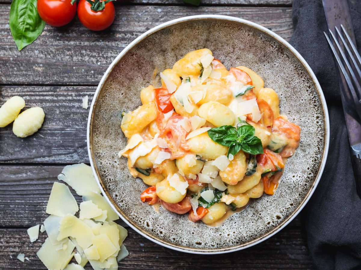 Frisch zubereitete Gnocchi in einer cremigen Tomaten-Sahne-Sauce mit Basilikum, serviert auf einem tiefen, rustikalen Teller.