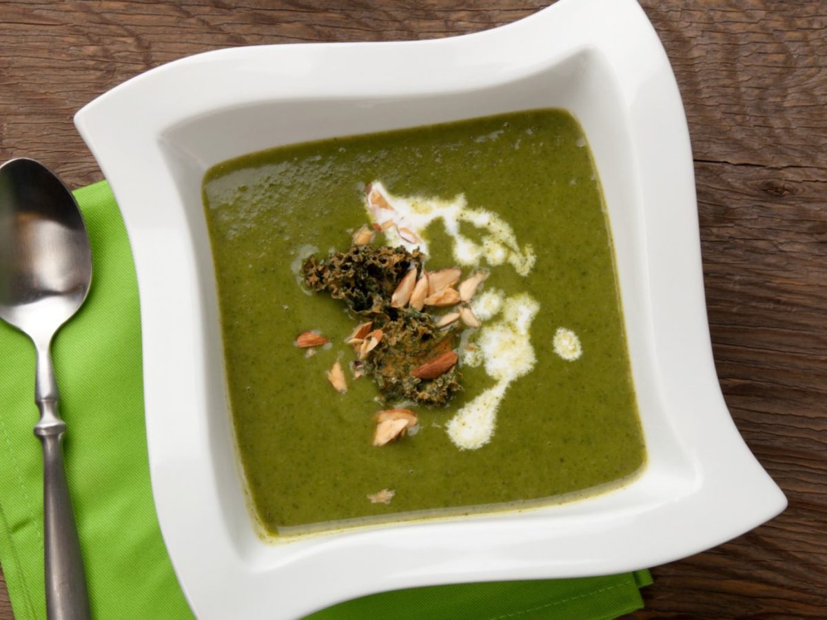 Pürierte Grünkohlsuppe mit Kartoffeln mit Topping auf Holztisch.