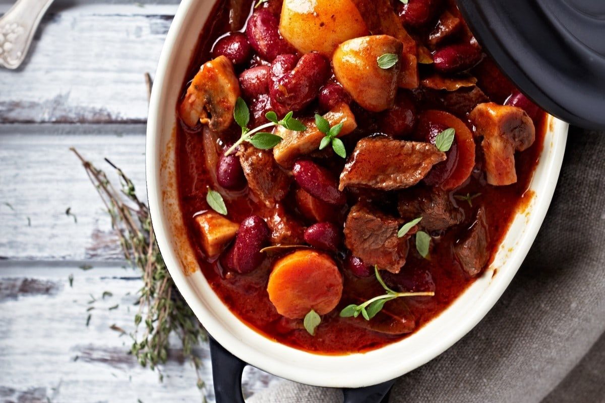 Rustikaler Hirtentopfs, reich gefüllt mit Fleisch, Pilzen und Kidenybohnen. Die Zutaten sind in einer herzhaften Sauce gekocht und präsentieren sich einladend in einem Kochtopf.