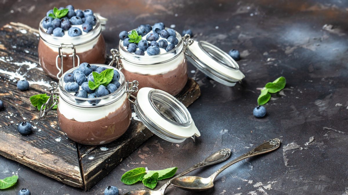 Draufsicht schräg: Drei Gläser mit Kokos-Schoko-Mousse mit Beeren. Die Gläser haben einen Deckel, der geöffnet ist.