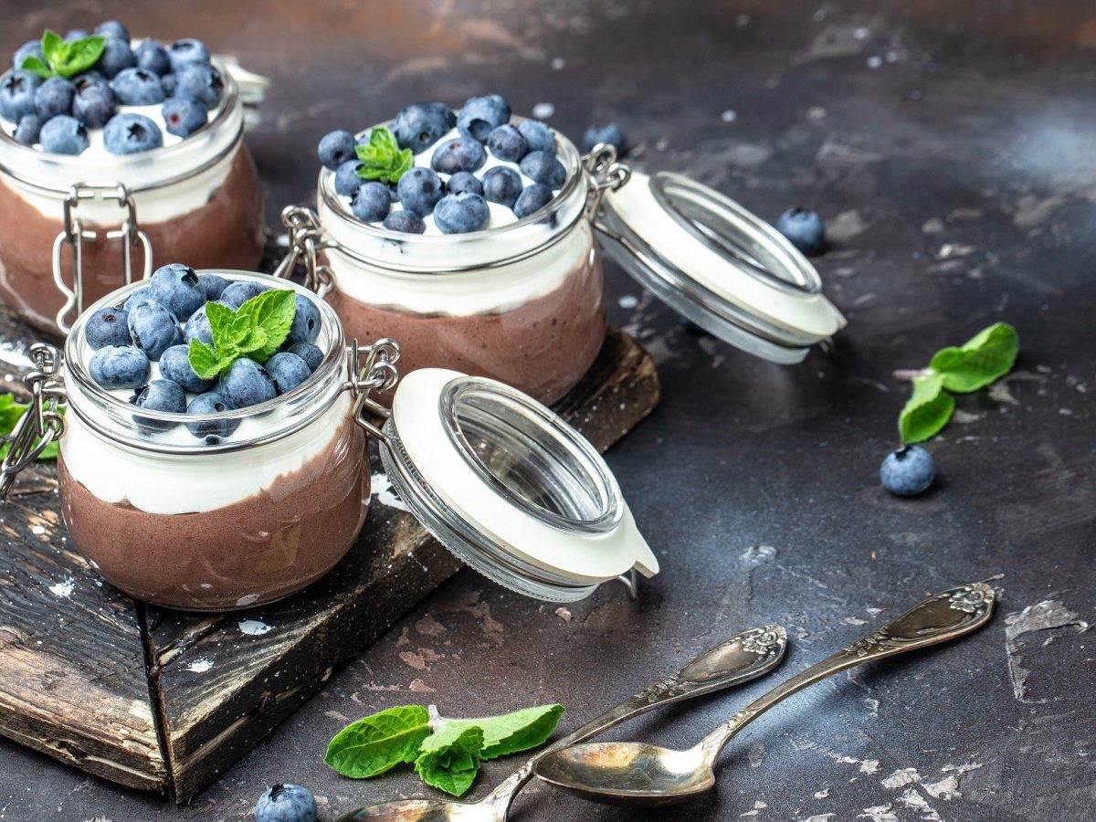 Draufsicht schräg: Drei Gläser mit Kokos-Schoko-Mousse mit Beeren. Die Gläser haben einen Deckel, der geöffnet ist.