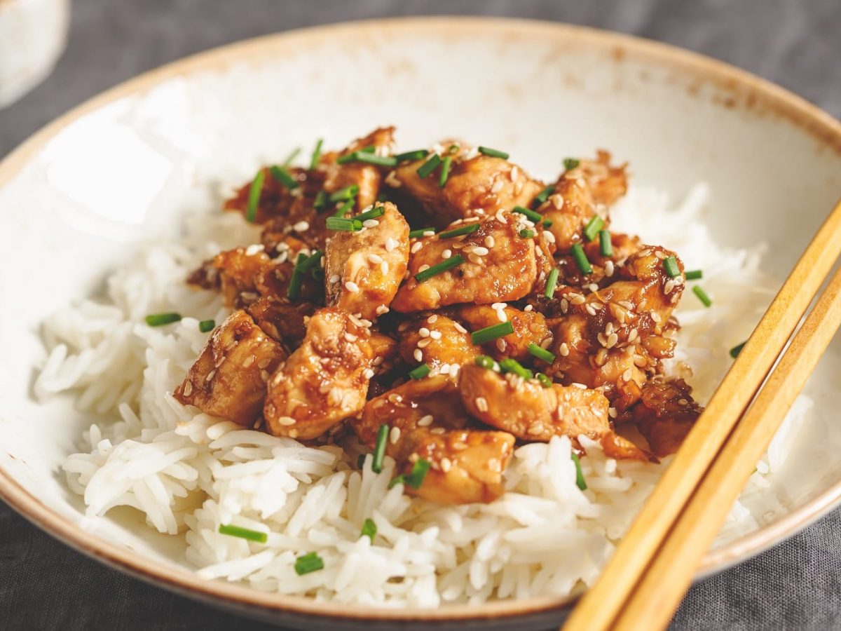 Ein weißer Teller mit dem Miso-Chicken und Reis auf einem grauen Untergrund.