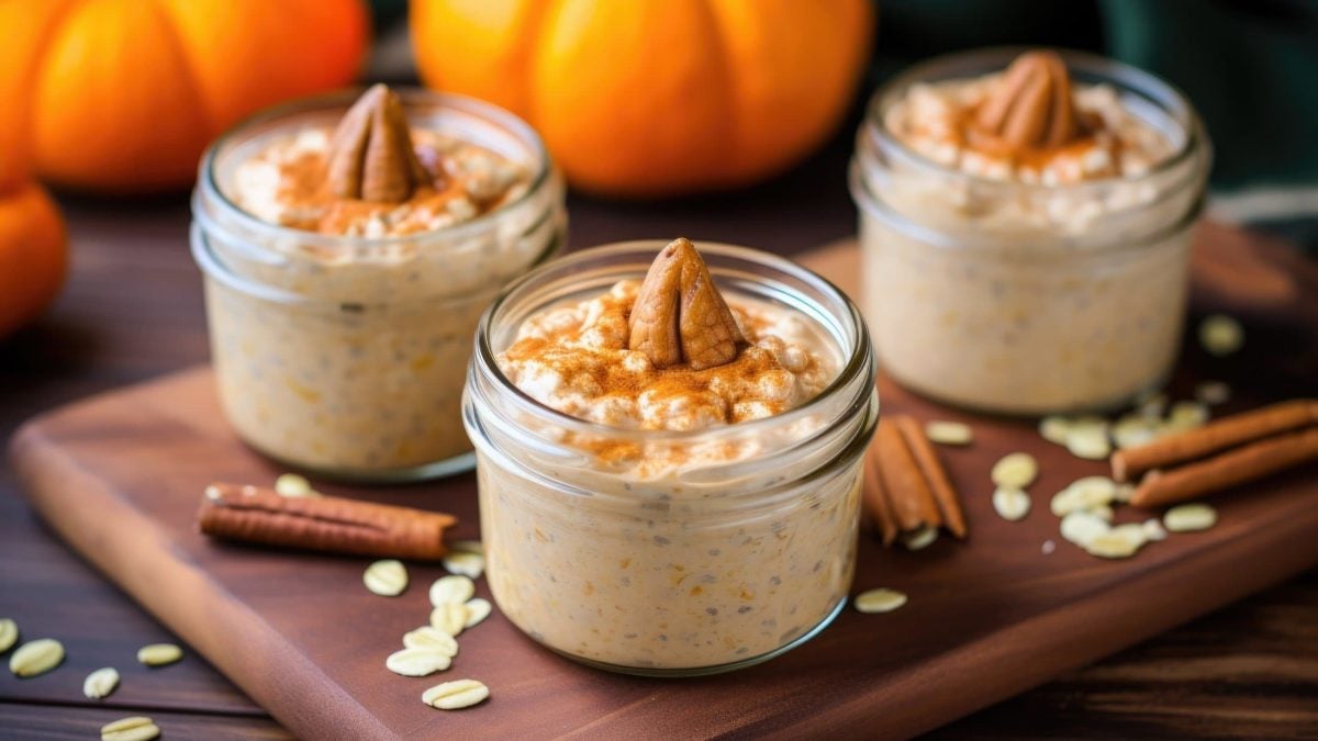 Frontal: Drei Gläser Overnight Oats mit Kürbis und Nüssen. Im Hintergrund liegen zwei Kürbisse.