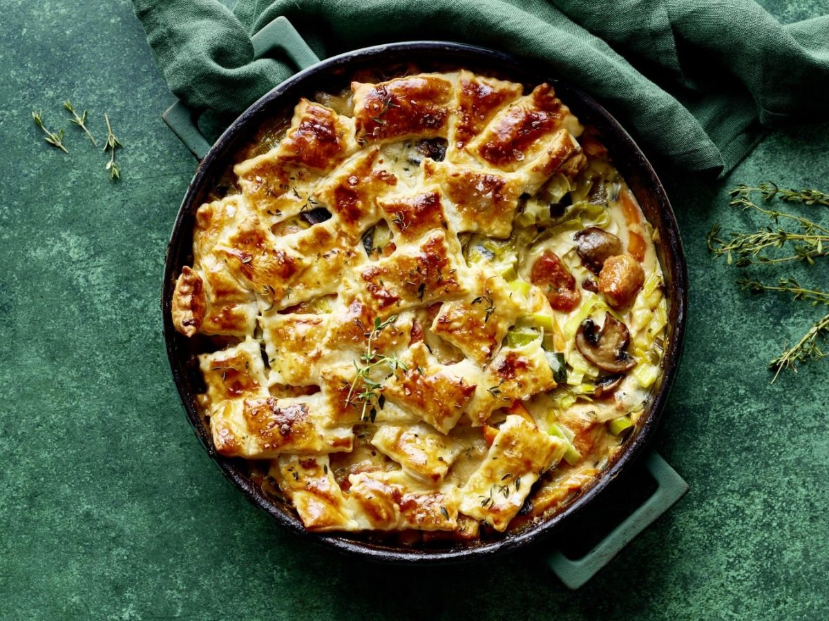 Eine Patchwork-Casserole mit Hähnchen-Lauch-Ragout auf grünem Hintergrund. Oben ein grünes Geschirrtuch. Links und rechts Thymian-Stiele.