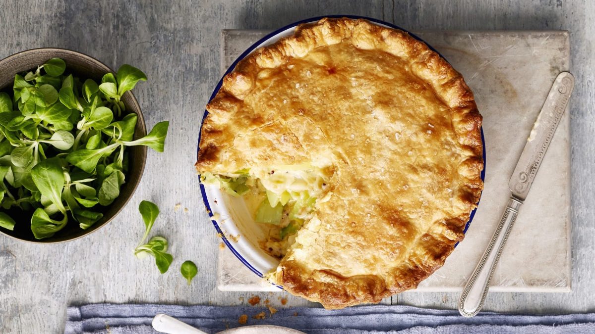 Angeschnittener Pie mit Kartoffel-Lauch-Füllung auf grauem Untergrund, daneben Schüssel mit Feldsalat.