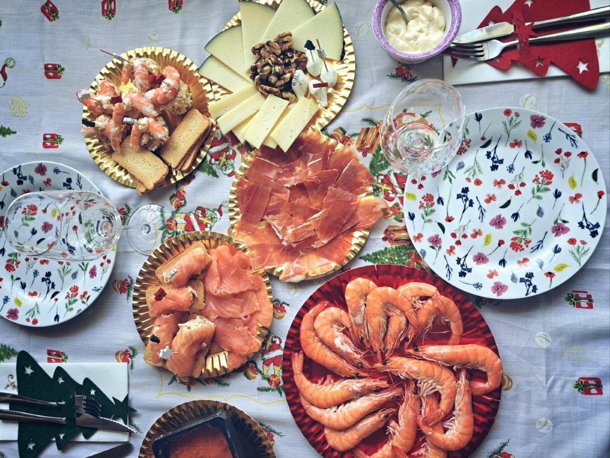 Spanisches Weihnachtsessen aus diversen Speisen auf Tellern und Häppchen auf gedecktem Tisch. Draufsicht.