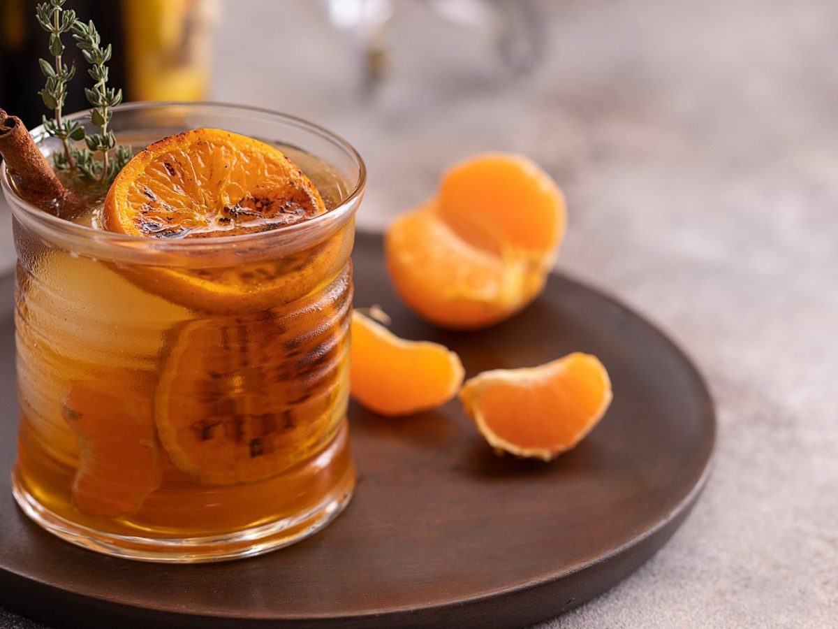 Ein Glas mit dem Drink auf einem braunen Teller mit Mandarinenstückchen.