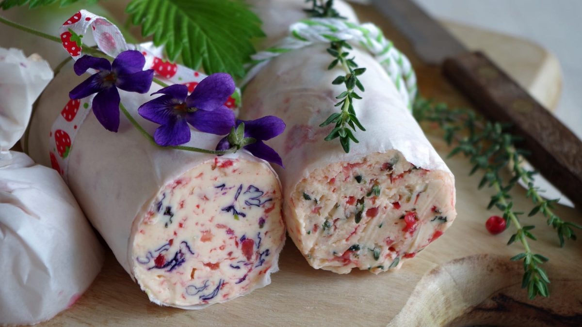 Zwei Rollen Cranberry-Butter auf einem Holzschneidebrett.