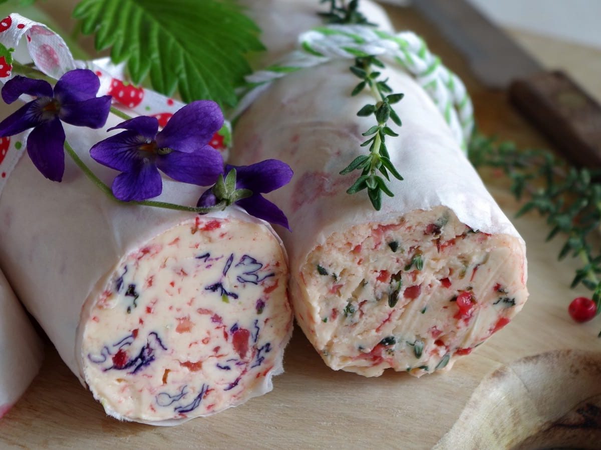 Zwei Rollen Cranberry-Butter auf einem Holzschneidebrett.