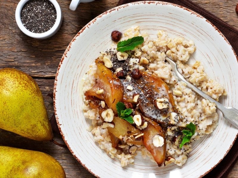 Ein weißer Teller mit karamellisiertem Birnen-Porridge auf einem braunen Holztisch.