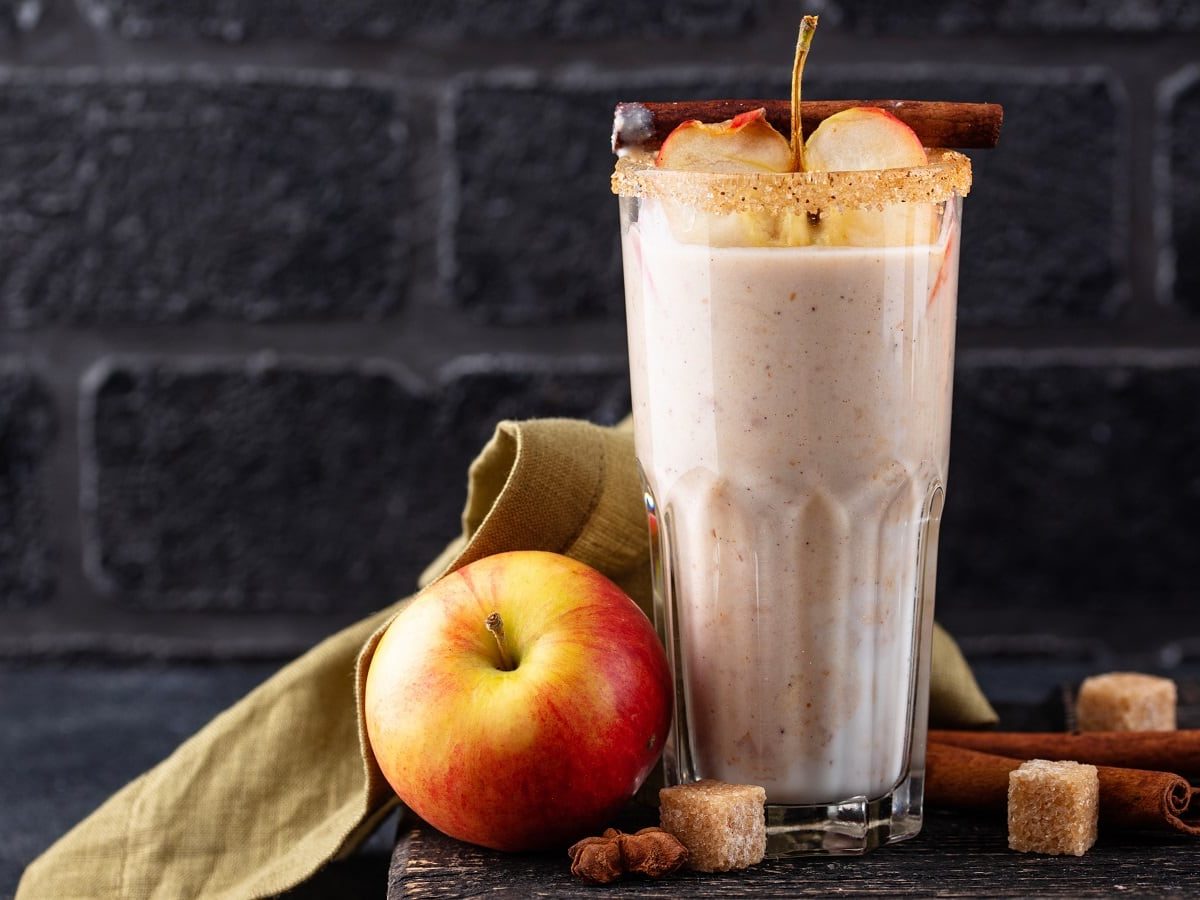 Ein Glas Apple Pie Smoothie vor einer dunkelgrauen Steinwand.