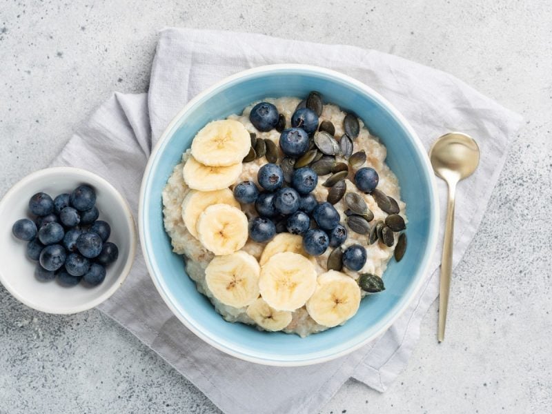 Eine blaue Schüssel Blueberry Cheesecake Porridge auf einem grauen Geschirrtuch.