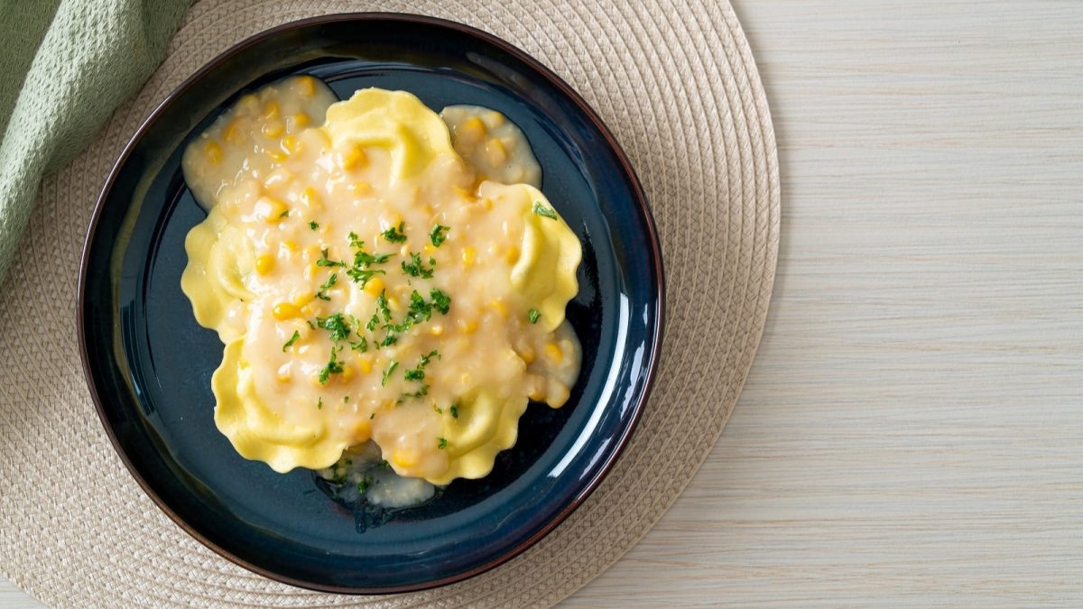 Ein dunkelblauer Teller mit Ravioli in Maiscreme auf einer Matte.