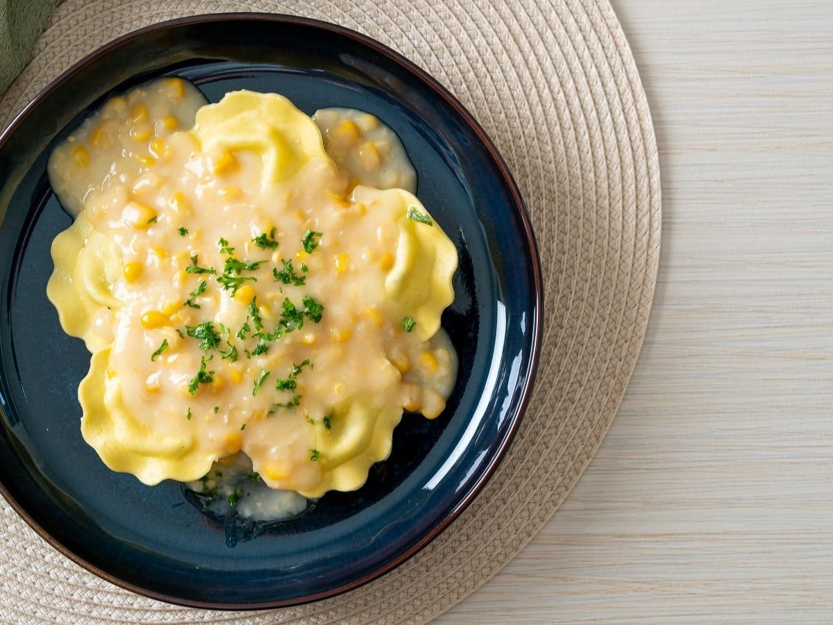 Ein dunkelblauer Teller mit Ravioli in Maiscreme auf einer Matte.