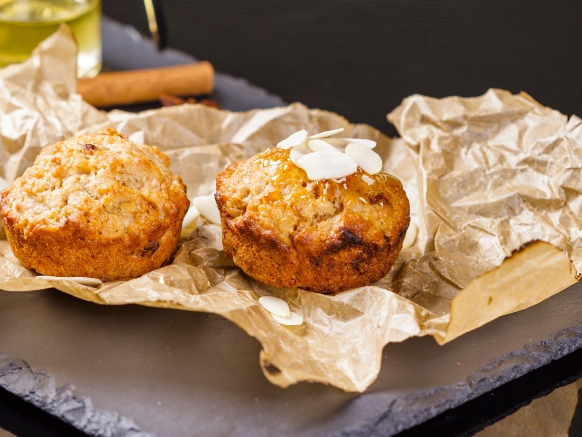 Zwei Apfel-Muffins auf einer schwarzen Schiefertafel mit Backpapier im Hintergrund.