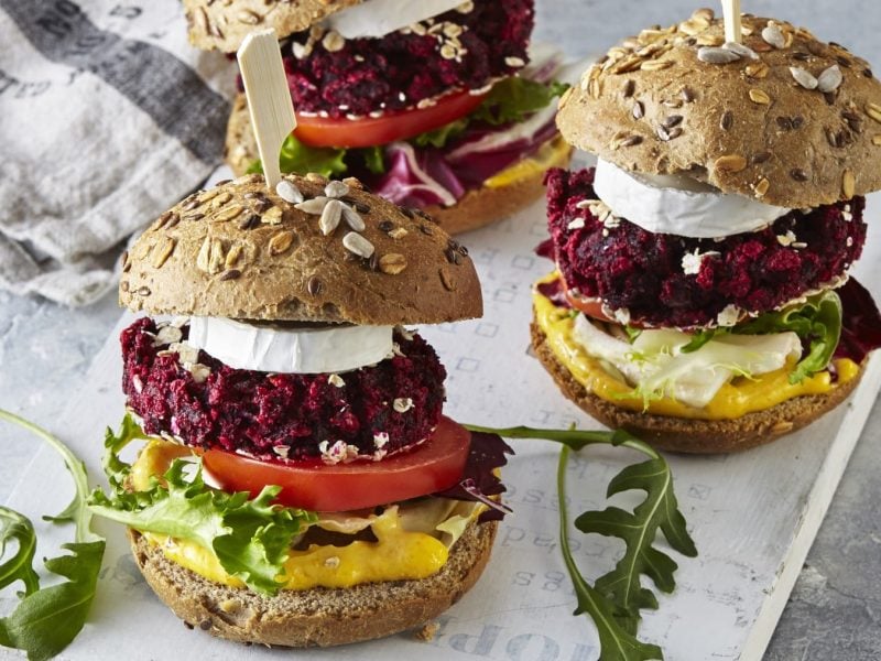 Drei Burger mit roter Bete und Ziegenkäse von vorne fotografiert auf einem grauen Schneidebrett auf einem grauen Hintergrund.