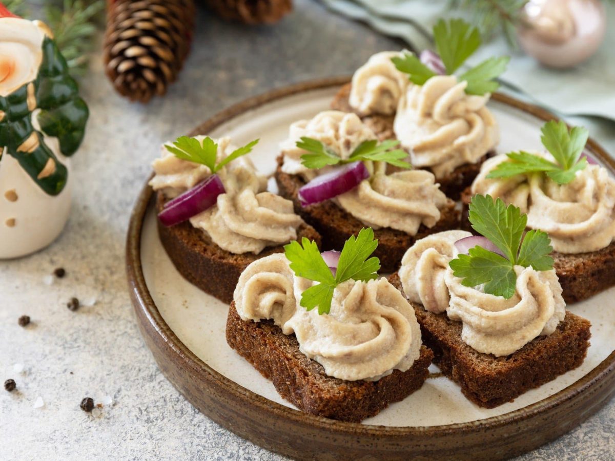 Draufsicht, schräg: Canapés mit Forellen-Creme auf einem beigen teller. Drum herum ist Weihnachts-Deko.