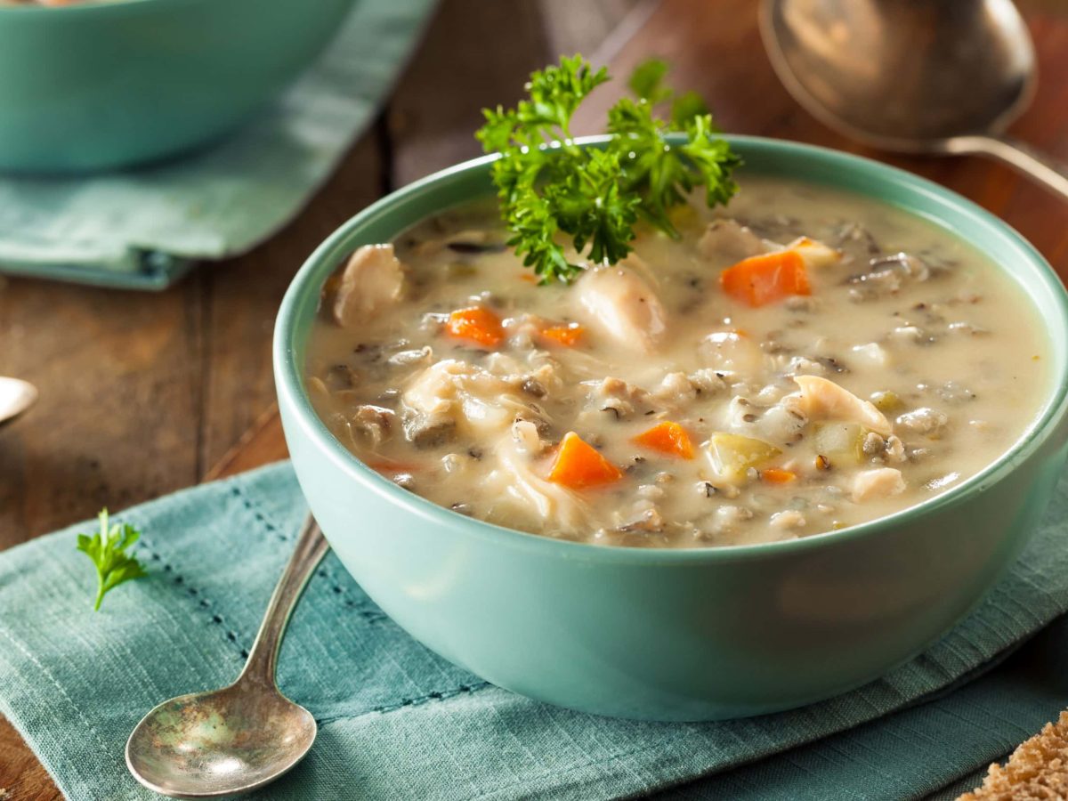 Eine türkisene Schale mit der Hühnersuppe auf einem dunklen Holztisch.