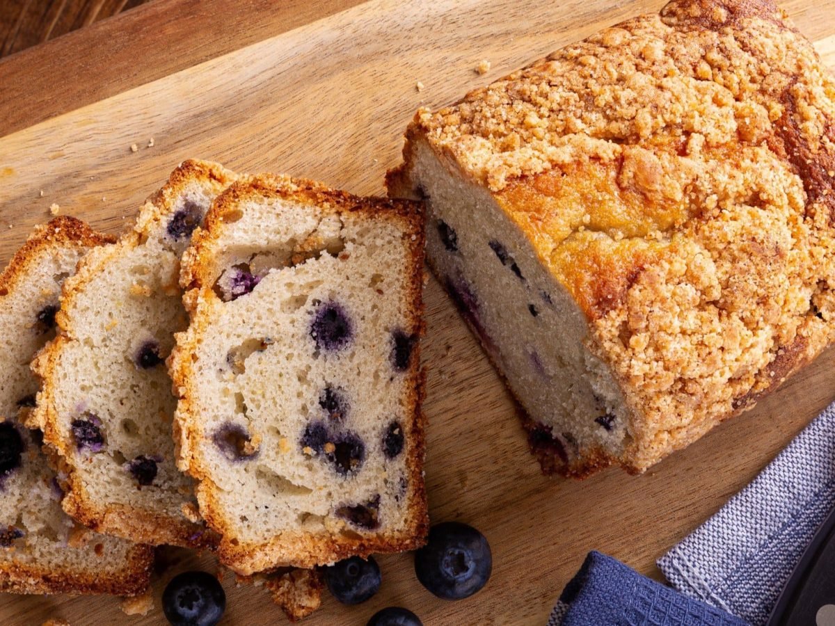 Draufsicht: Ein angeschnittenes Blaubeer-Brot auf einem Holzbrettchen.