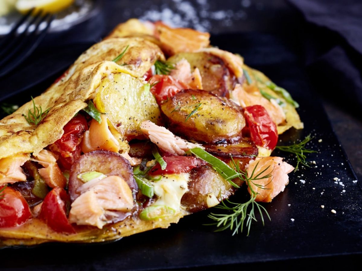 Ein schwarzer Teller mit einer Portion Fischerfrühstück mit Lachs auf einem dunklen Tisch.