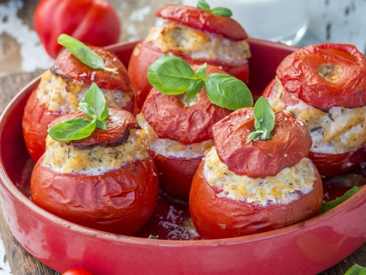 Fünf gefüllte Bulgur-Tomaten in einem roten tiefen Teller.