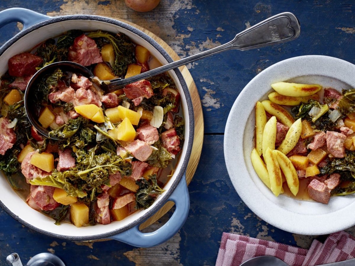 Ein Topf mit Kasseler-Gulasch, rechts davon ein Teller mit Kasseler-Gulasch und Schupfnudeln. Der Hintergrund ist blau.