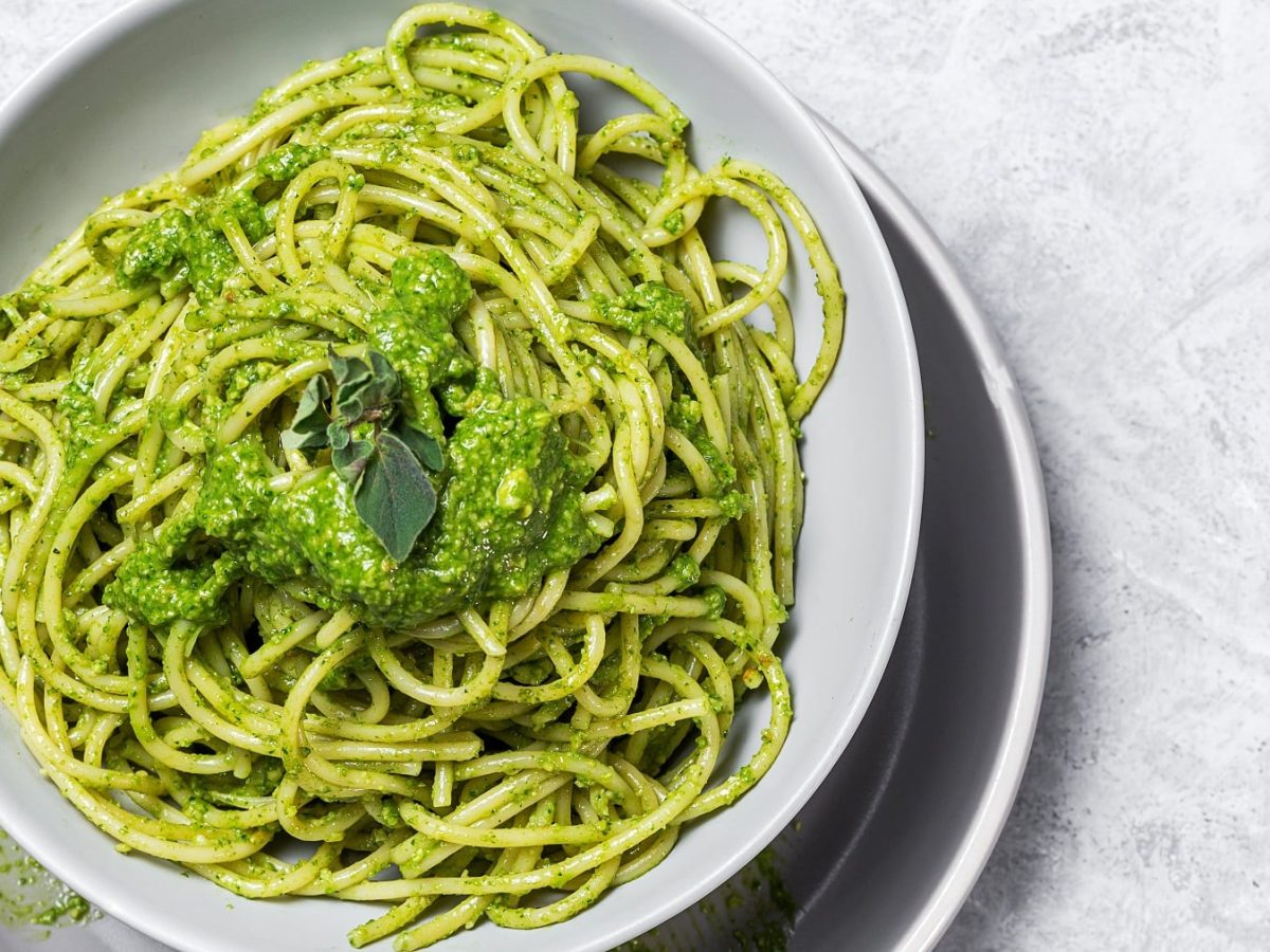 Pasta mit grüner Sauce auf einem grauen Tisch. Alles von oben fotografiert.