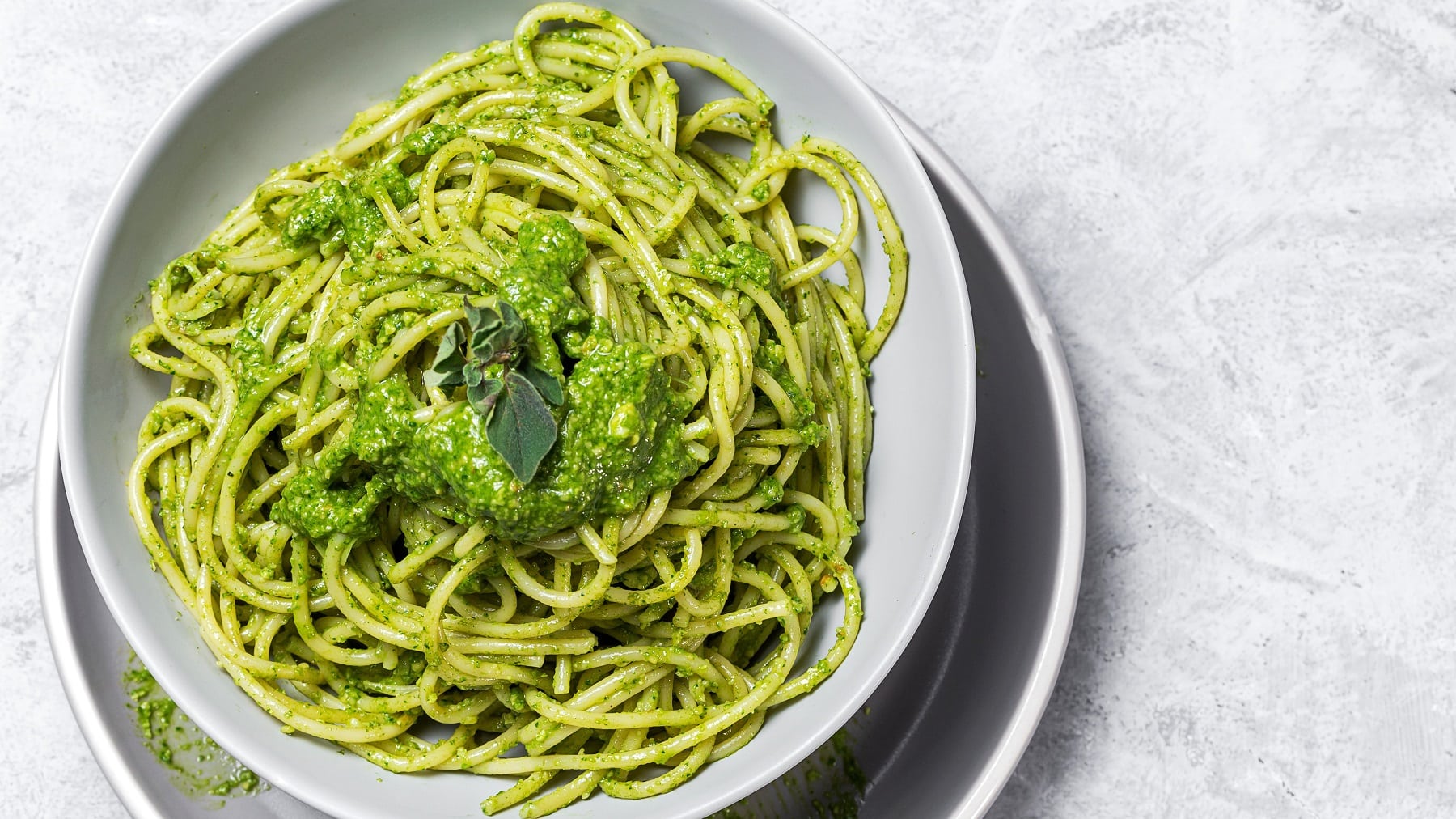 Pasta mit grüner Sauce auf einem grauen Tisch. Alles von oben fotografiert.