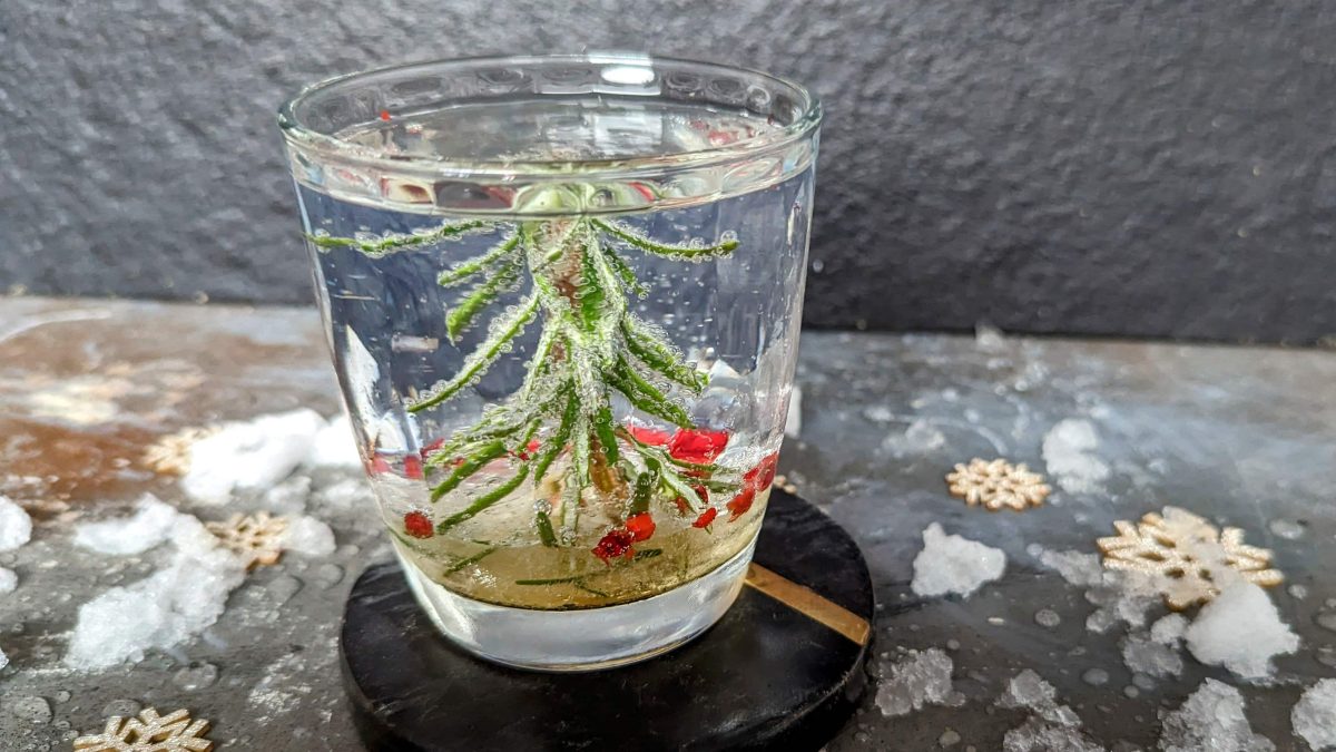 Ein Glas mit der weihnachtlichen Dekoration udn einem Gin Tonic auf einem Steintisch mit schwarzem Hintergrund. Nah und von der Seite fotografiert.