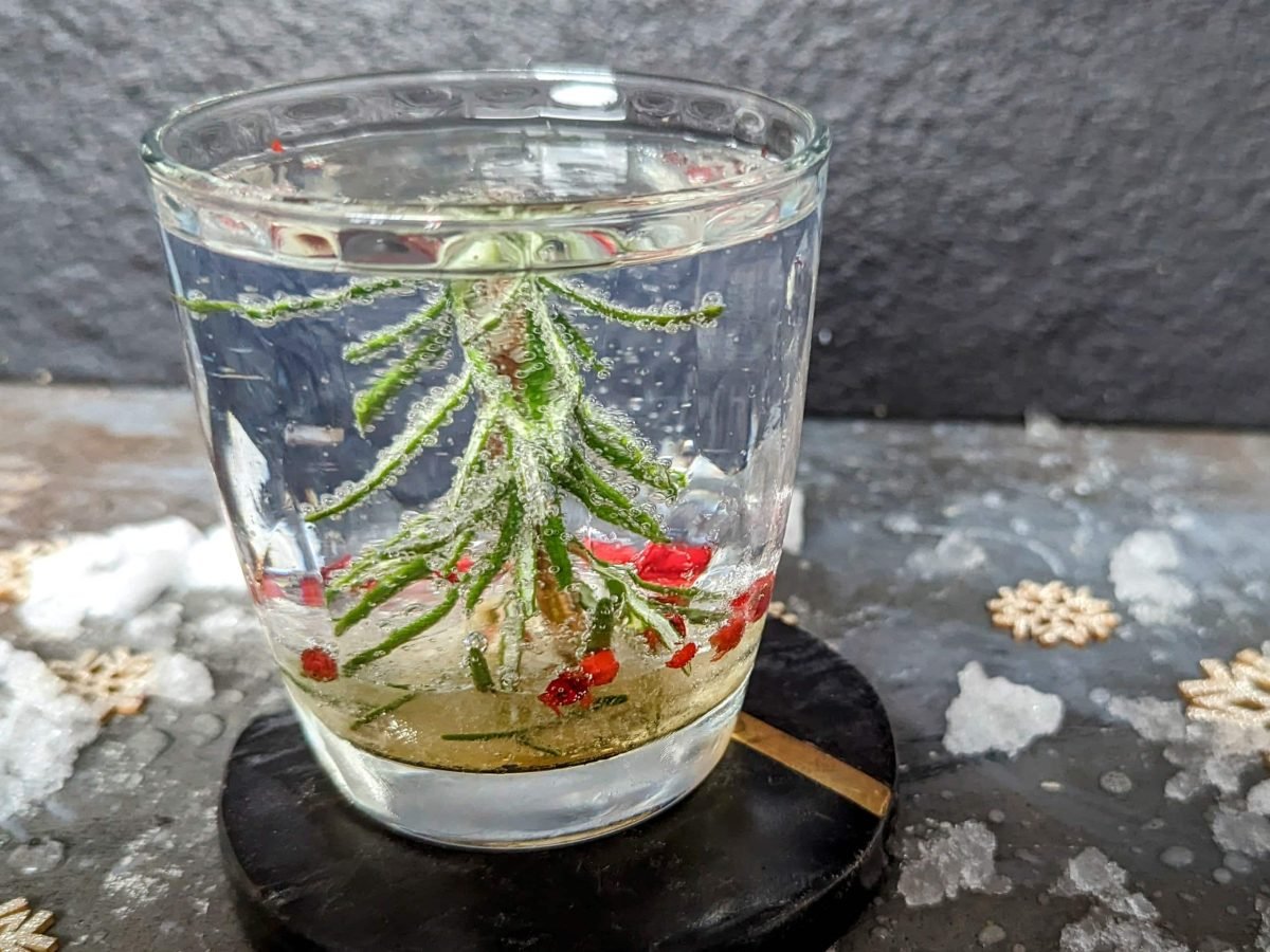 Ein Glas mit der weihnachtlichen Dekoration udn einem Gin Tonic auf einem Steintisch mit schwarzem Hintergrund. Nah und von der Seite fotografiert.