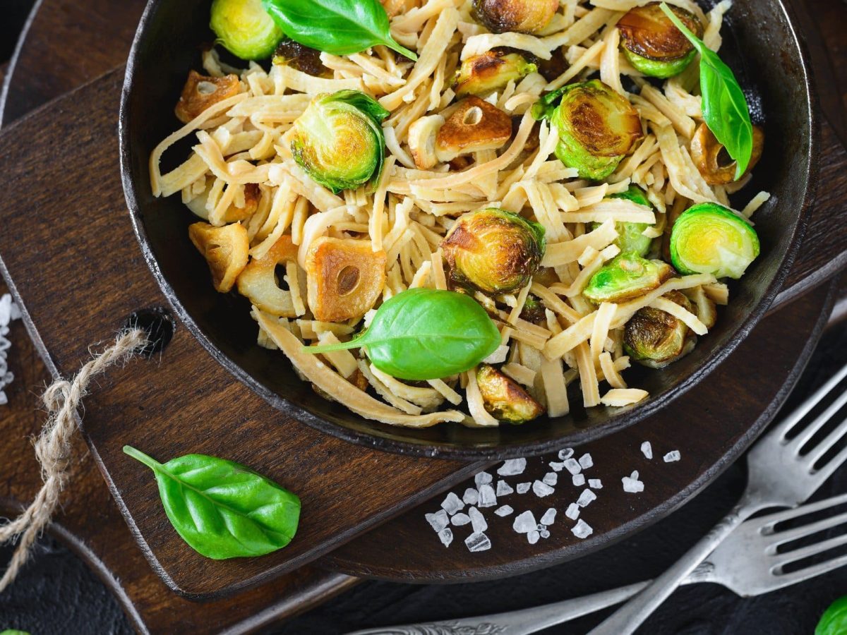 Draufsicht: Eine Rosenkohl-Pasta mit gebratenem Knoblauch. Drum herum liegen grobe Salzkörner und frische Basilikumblätter.