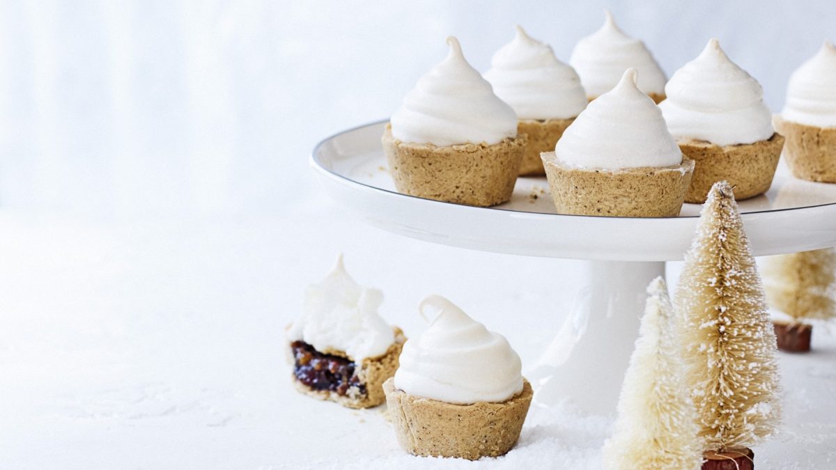 Schneehäubchen-Pies auf einem weißen Servierteller auf einem weißen Hintergrund. Vor dem Servierteller stehen kleine Tannenbäume als Weihnachtsdekoration.