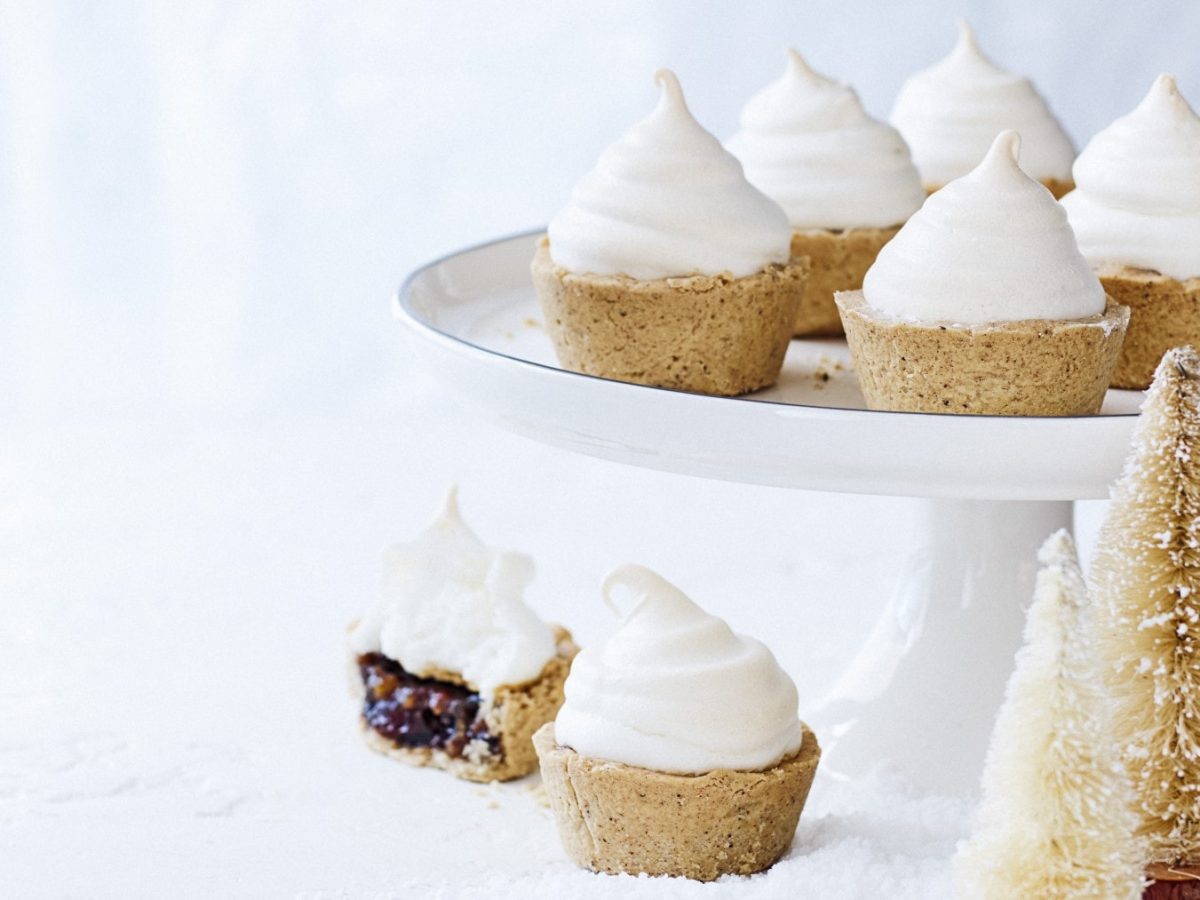 Schneehäubchen-Pies auf einem weißen Servierteller auf einem weißen Hintergrund. Vor dem Servierteller stehen kleine Tannenbäume als Weihnachtsdekoration.