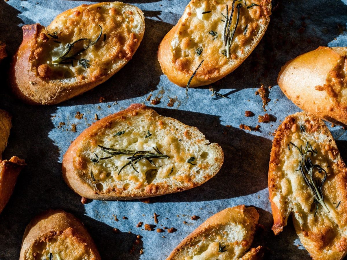 Draufsicht: Mehrere überbackene Käse-Knoblauch-Bruschetta auf blauem Untergrund.