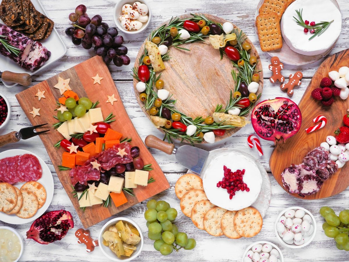 Weihnachtliche Charcuterie-Tischszene auf einem weißen Holzhintergrund. Diverse Käse- und Fleischvorspeisen. Weihnachtsbaum, Kranz und süße Arrangements.